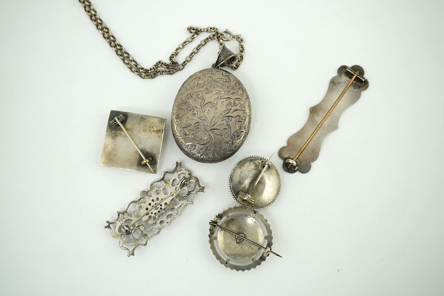 An oval engraved white metal enclosed locket and chain and five assorted white metal brooches. Condition - fair